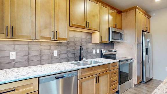 Kitchen corner with sink, stainless steel appliances, and natural wood upper and lower cabinets.