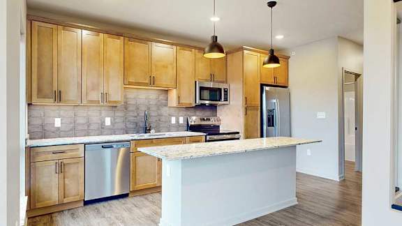 Kitchen with natural wood cabinetry, quartz countertops, stainless steel appliances, and pendant lighting over the island.