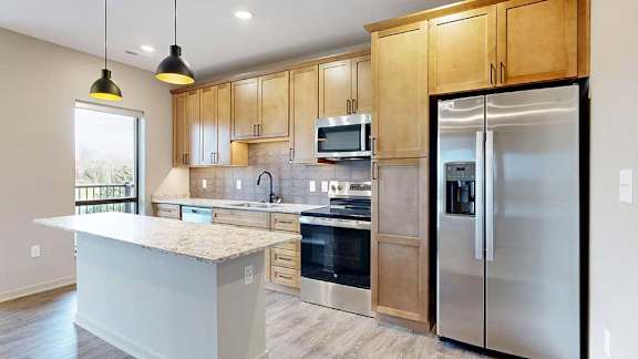 a modern kitchen featuring wood cabinets, stainless steel appliances, and two pendant lights above the island