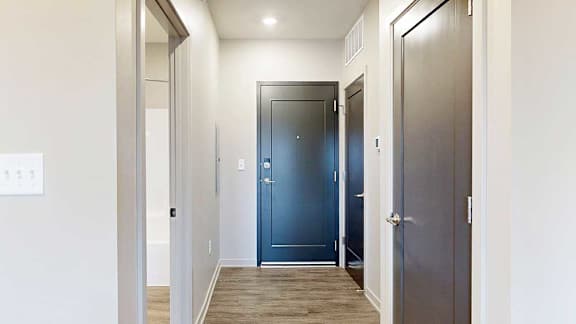 Front door view with wooden vinyl flooring, flanked by doorways to bathroom and coat closet.