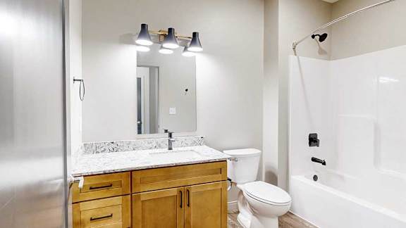A bathroom with a wooded vanity, quartz countertop, a large mirror, and overhead light fixtures.