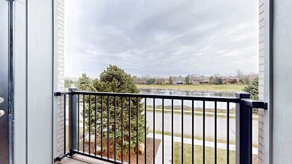 Balcony view with black railing overlooking a tree-lined street and open sky.