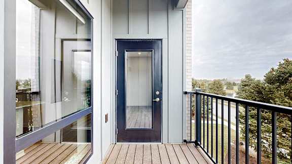 Balcony entrance with glass-panel door and wood-style flooring, adjacent to interior windows.