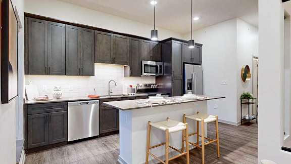 a kitchen with dark cabinets, tile backsplash, and stainless steel appliances