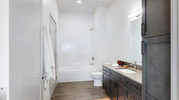 A walk-through bathroom with a wide quartz vanity and a white tub shower.