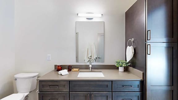 A bathroom with a quartz vanity, dark wooden cabinets, and a tall storage cabinet.