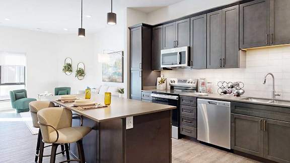 a modern kitchen with a stainless steel appliances, quartz countertops, a light tile backsplash, dark wooden cabinets, and a large central island