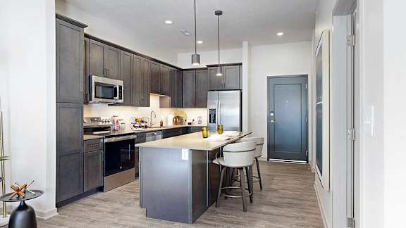 A kitchen with dark wooden cabinets, quartz countertops, an island, and stainless steel appliances.