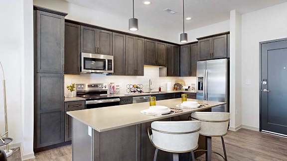 a modern kitchen with a stainless steel appliances, quartz countertops, a light tile backsplash, dark wooden cabinets, and a large central island