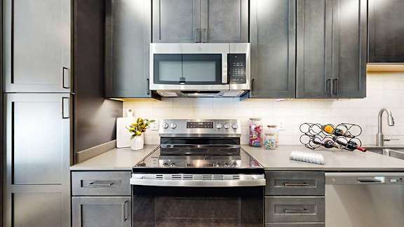 a modern kitchen with a stainless steel appliances, quartz countertops, a light tile backsplash, and dark wooden cabinets