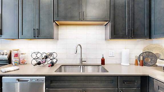 A modern kitchen sink with quartz counters, dark wooden cabinets, and a tile backsplash.