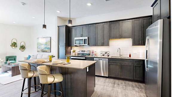 A kitchen with dark wooden cabinets, quartz countertops, an island, and stainless steel appliances.