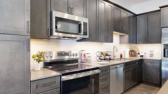 a modern kitchen with a stainless steel appliances, quartz countertops, a light tile backsplash, and dark wooden cabinets