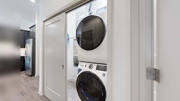 a white and black stackable full-size washer and dryer in a double door closet in the front hallway