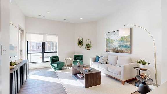 A living room with a white couch, two green arm chairs, and several modern furnishings.