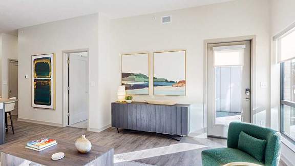 A living room with a green chair, a TV stand, and several paintings.