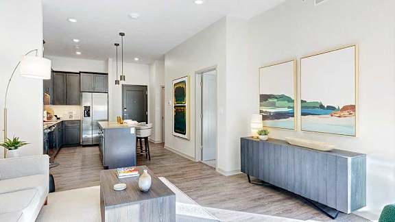 A living room with hardwood-style flooring and kitchen with dark wooden cabinets.