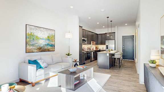 a furnished living room with midcentury modern furniture and decor next to an open kitchen area with an island and dark cabinets
