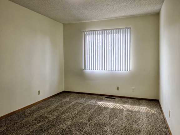 A carpeted bedroom with a window with blinds.