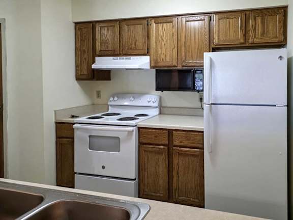 A kitchen with wooden cabinets, white appliances, and a mounted microwave.