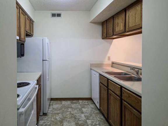 A kitchen with wooden cabinets, white appliances, and a passthrough counter top open to the living room.