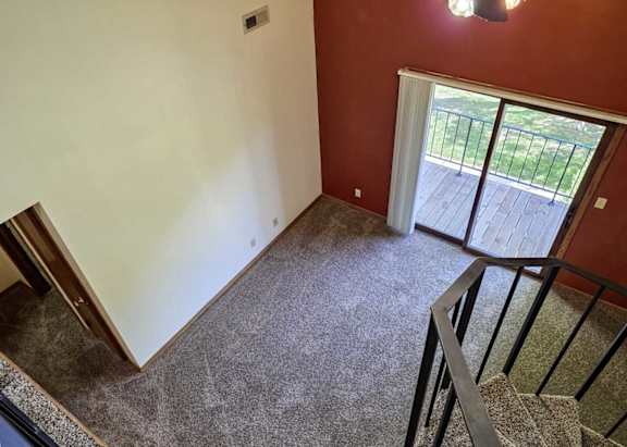 A view of a living room with a red accent wall and a sliding glass door to a balcony, from a loft area.