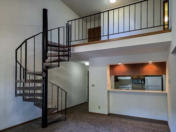 A living room with a pass through counter to the kitchen, and a spiral staircase with a metal railing to the loft area above.