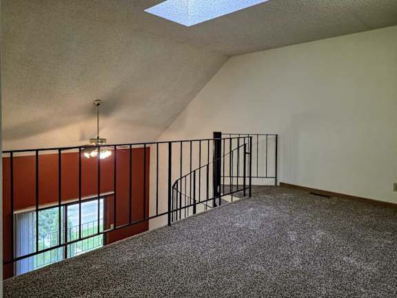 A loft area with a black metal railing, a spiral staircase down to the living room below, and a sky light.