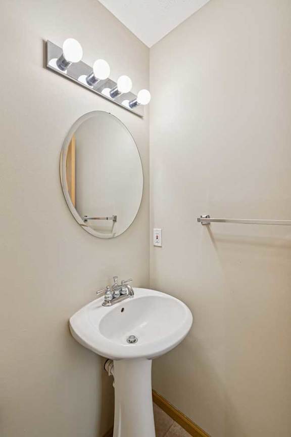 A white pedestal sink under a round mirror with lights above it.