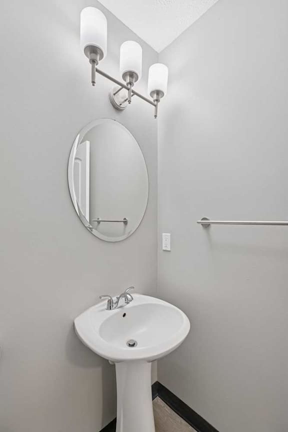 A white pedestal sink with a round mirror above it.