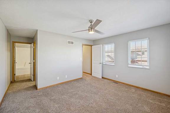 A room with a ceiling fan and two windows.
