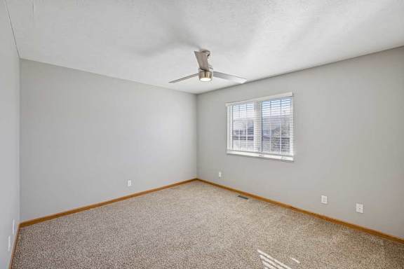 A room with a ceiling fan and a window with blinds.