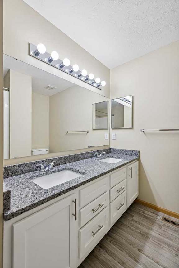 A bathroom with a granite countertop and a vanity with a sink and mirror.