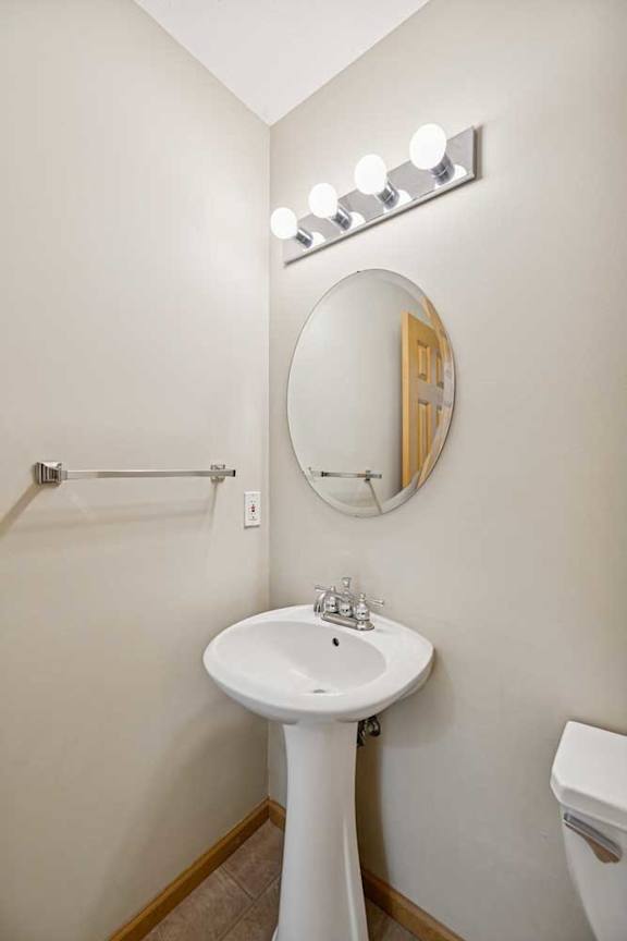 A white pedestal sink under a round mirror with lights above it.