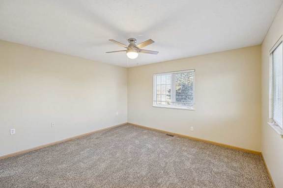 A room with a ceiling fan and a window with a view of trees.