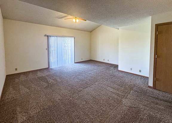a living room with carpeted floor and a sliding glass door with blinds