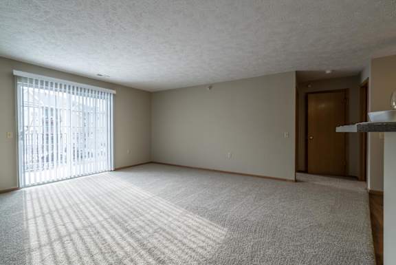 A living room with a carpeted floor and a sliding glass door with vertical blinds