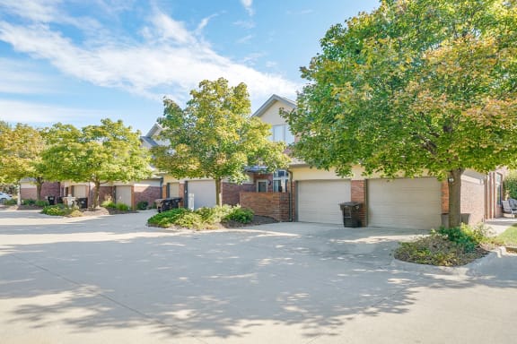 the exteriors of a row of villas with attached garages and trees lining the road