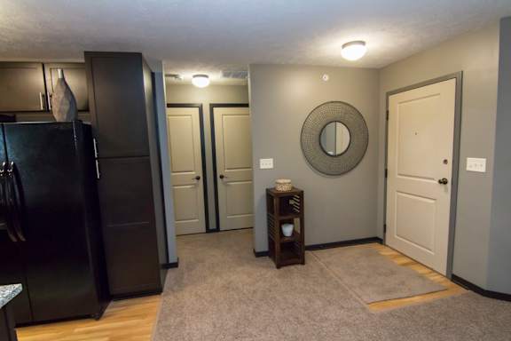 A black refrigerator stands in a kitchen with a grey wall and a round mirror on the wall.