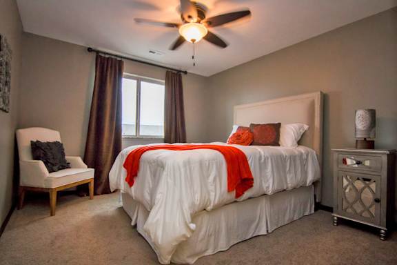 A bedroom with a bed, chair, and window.