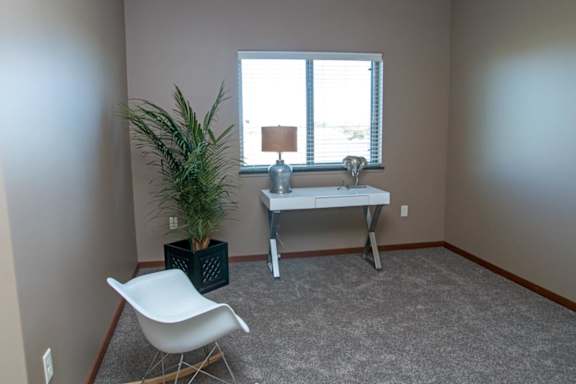 A room with a white chair, a desk, and a plant.