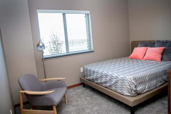 A bedroom with a bed, chair, and window.