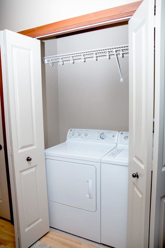 A white washer and dryer in a small laundry closet with storage shelf above it