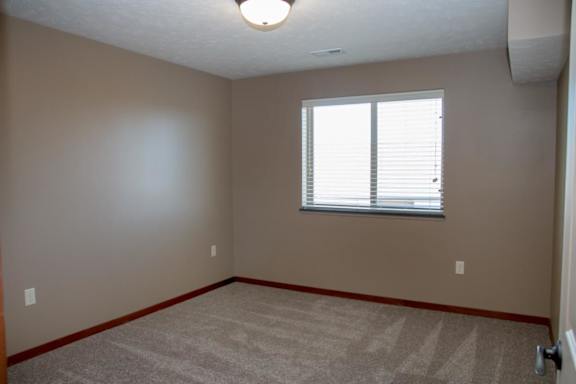 A room with a carpeted floor and a window with blinds.