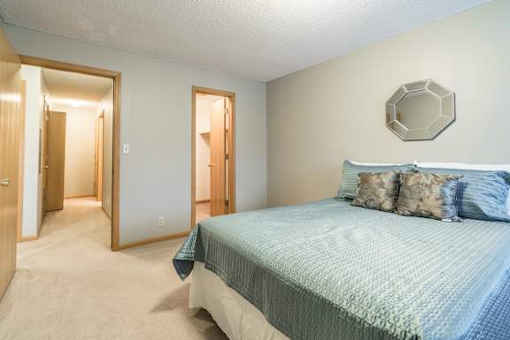A bedroom with a bed and a mirror on the wall and a door to the walk-in closet