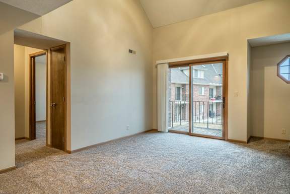 Apartment living room with a carpeted floor and a sliding glass door leading to a balcony.