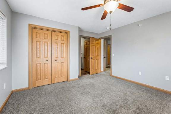 Carpeted bedroom with ceiling fan and double closet doors.