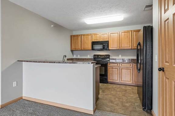 Open apartment kitchen with wood-tone cabinets, black oven and microwave, granite-look laminate countertops, and ample cabinet storage in a functional layout.