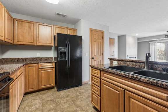 A kitchen with a black refrigerator and wooden cabinets.