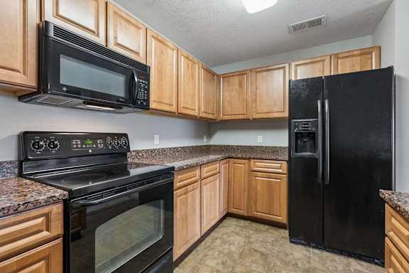 A black refrigerator sits in a kitchen with wooden cabinets.